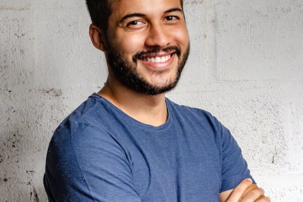 portrait photo of smiling man with his arms crossed standing in front of a wall
